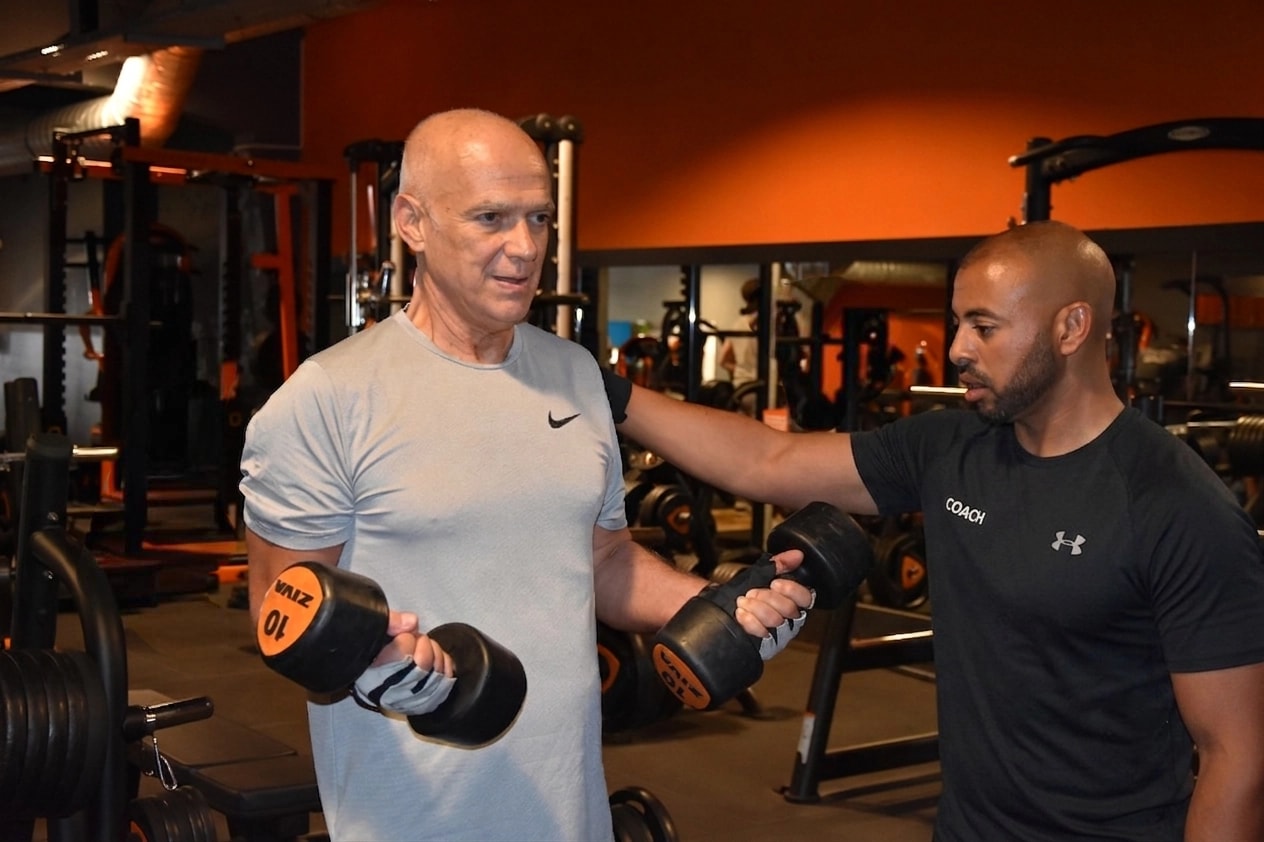 Coach sportif encadrant un exercice de biceps en salle